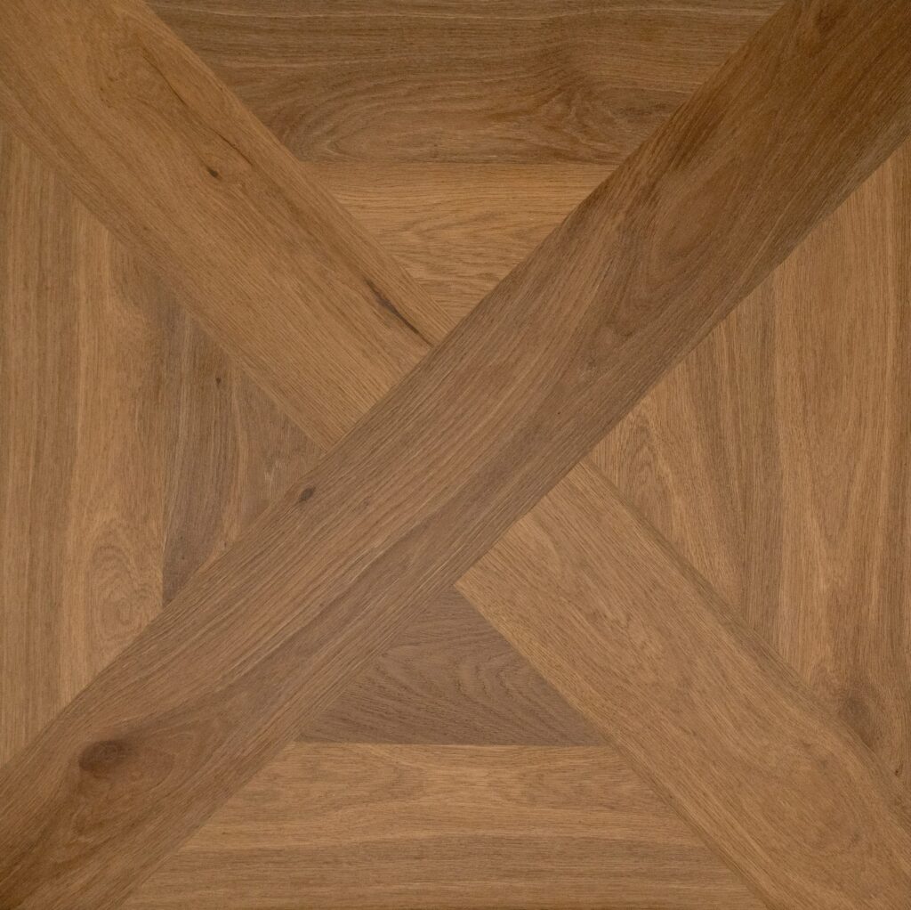 Close-up of a wooden parquet floor pattern with warm medium-brown planks arranged in an X and geometric design.